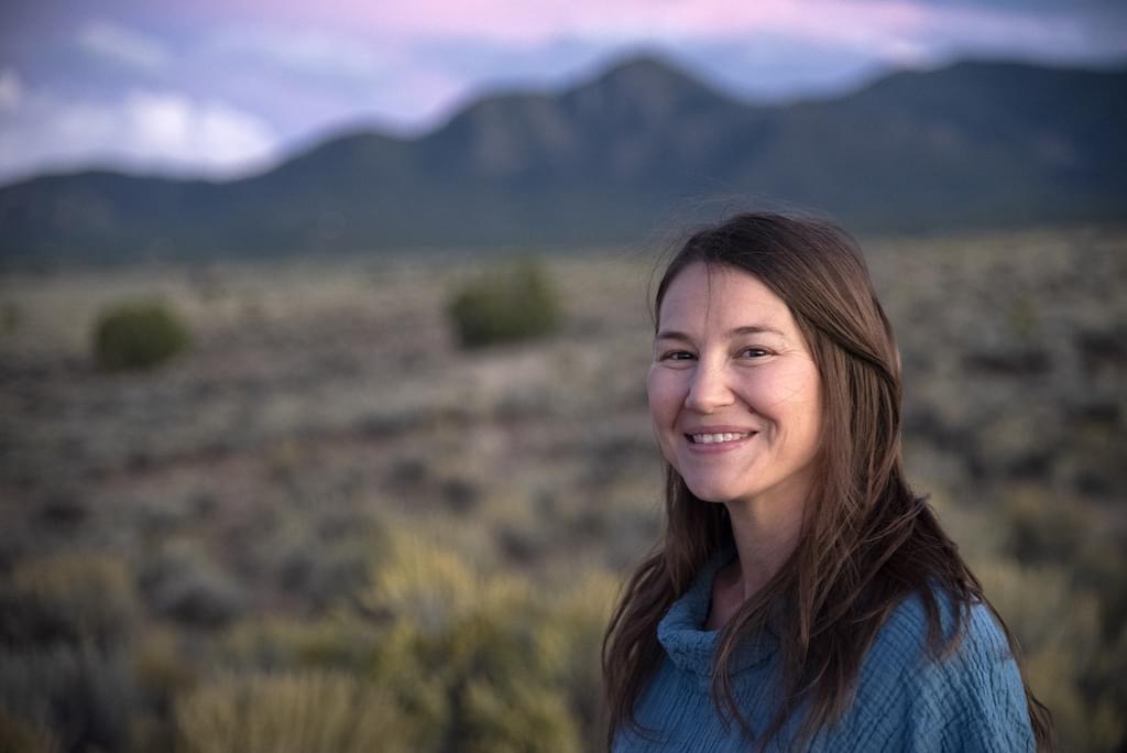 A smiling woman standing in front of distant mountains