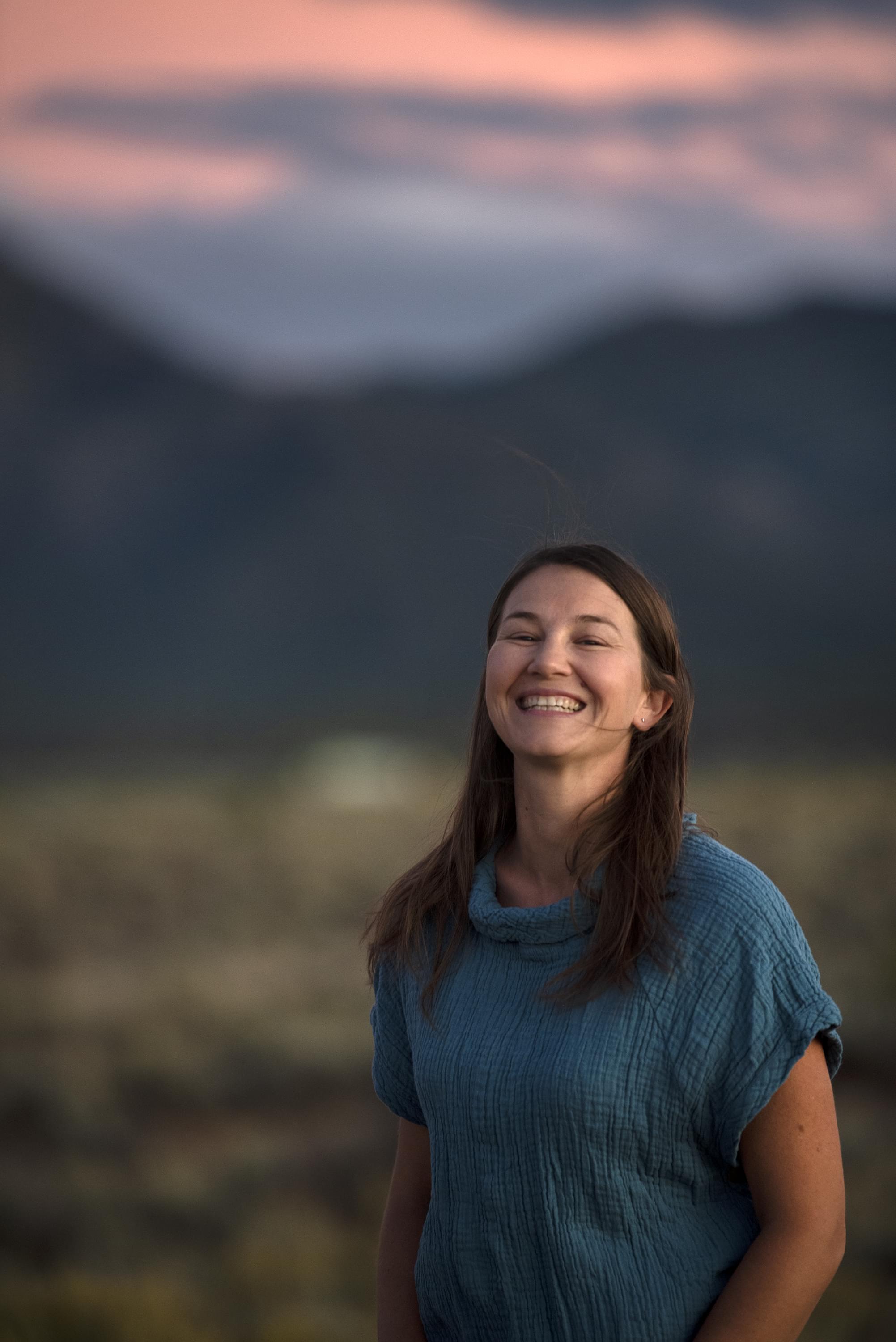 A smiling woman standing outside in a moutainous desert near sunset
